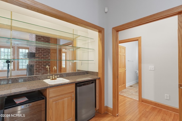 bar featuring dishwasher, light wood-type flooring, dark stone counters, and sink