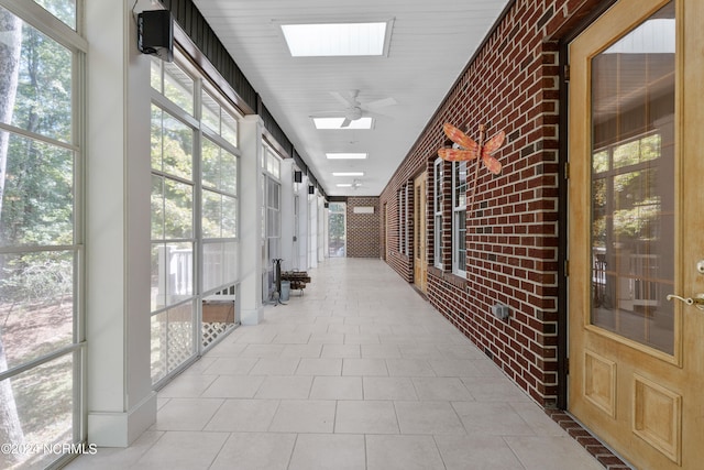 hallway featuring a skylight, light tile patterned flooring, and brick wall