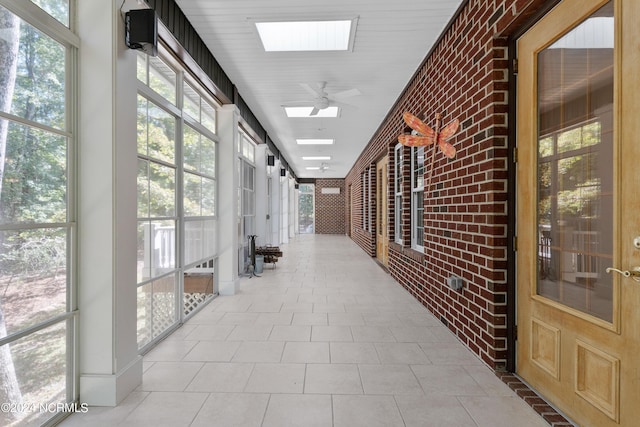 hallway featuring tile patterned floors, brick wall, and a skylight