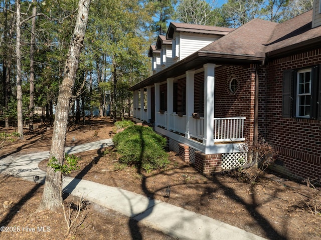 view of side of home featuring crawl space, covered porch, brick siding, and a shingled roof