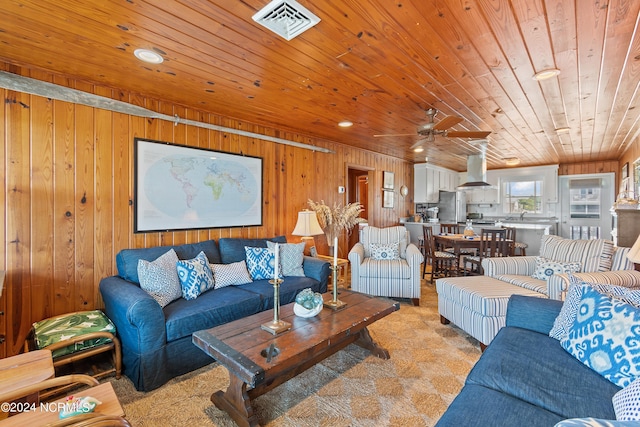 living room featuring ceiling fan, wooden walls, light carpet, and wood ceiling