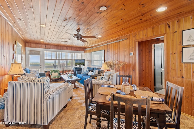 carpeted dining area featuring ceiling fan, wood walls, and wooden ceiling