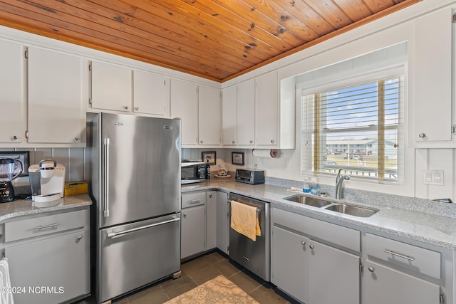 kitchen with appliances with stainless steel finishes, sink, white cabinets, dark tile patterned flooring, and wooden ceiling