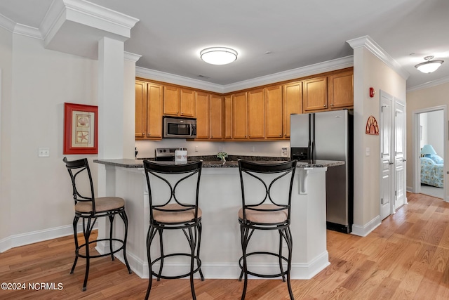 kitchen with crown molding, a kitchen bar, dark stone counters, and stainless steel appliances