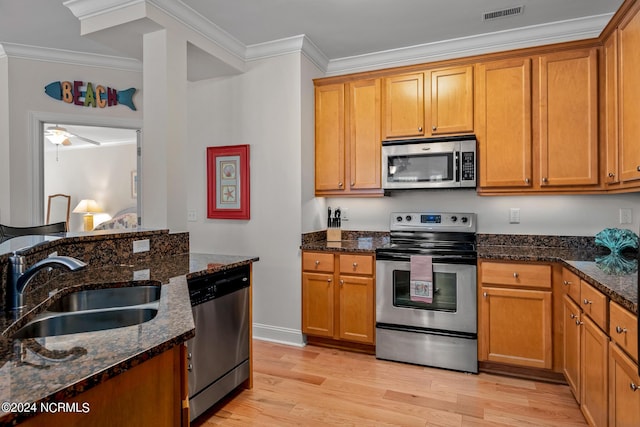 kitchen featuring sink, stainless steel appliances, dark stone counters, and crown molding