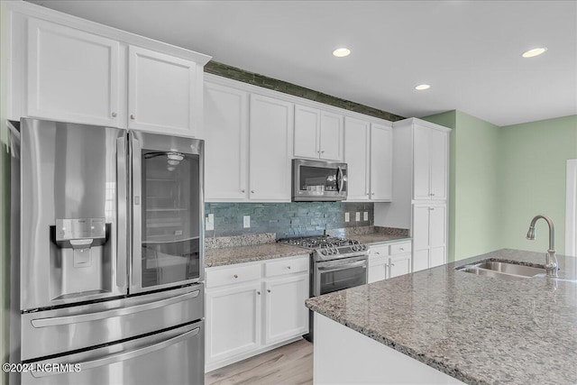 kitchen with appliances with stainless steel finishes, sink, decorative backsplash, light wood-type flooring, and white cabinetry