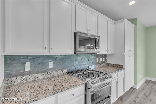 kitchen featuring appliances with stainless steel finishes, white cabinets, light stone counters, decorative backsplash, and light wood-type flooring