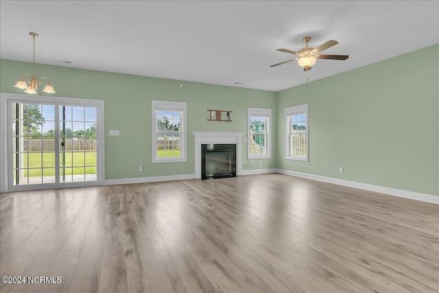 unfurnished living room with hardwood / wood-style flooring, ceiling fan with notable chandelier, and a wealth of natural light