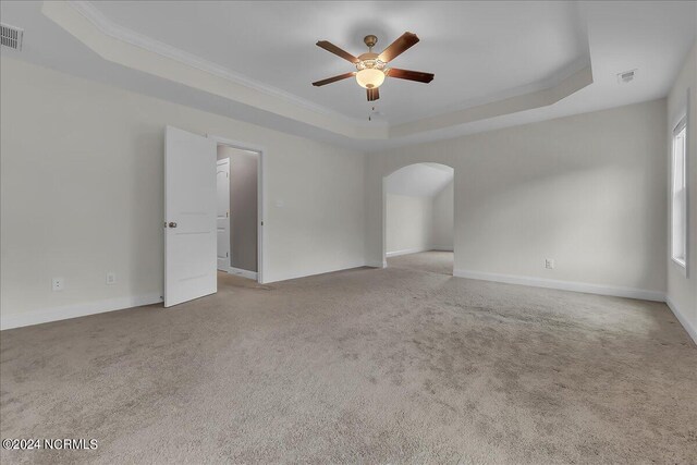 empty room with crown molding, ceiling fan, a raised ceiling, and carpet flooring