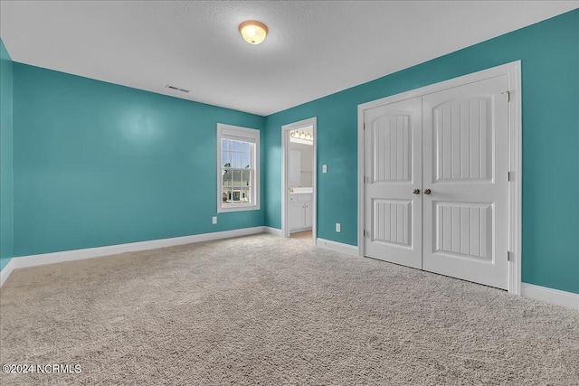 unfurnished bedroom with a closet, carpet floors, and ensuite bathroom