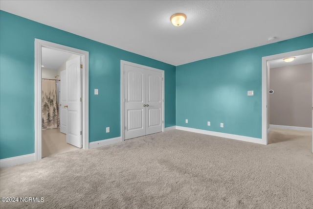 unfurnished bedroom featuring a closet, ensuite bath, and carpet flooring