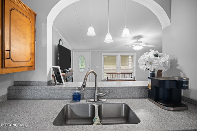 kitchen with arched walkways, brown cabinets, hanging light fixtures, a ceiling fan, and a sink