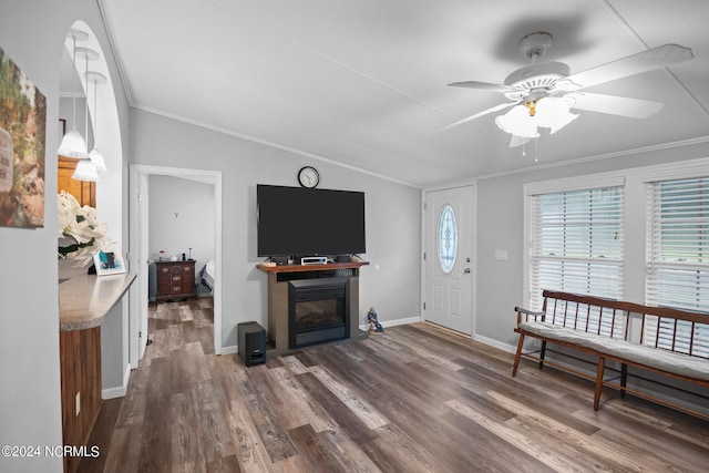 living area featuring dark wood-type flooring, a glass covered fireplace, vaulted ceiling, and ornamental molding