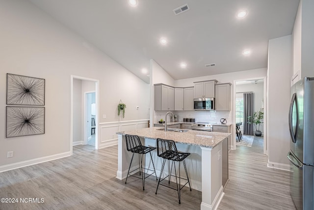 kitchen featuring a kitchen island with sink, gray cabinetry, sink, stainless steel appliances, and light stone countertops