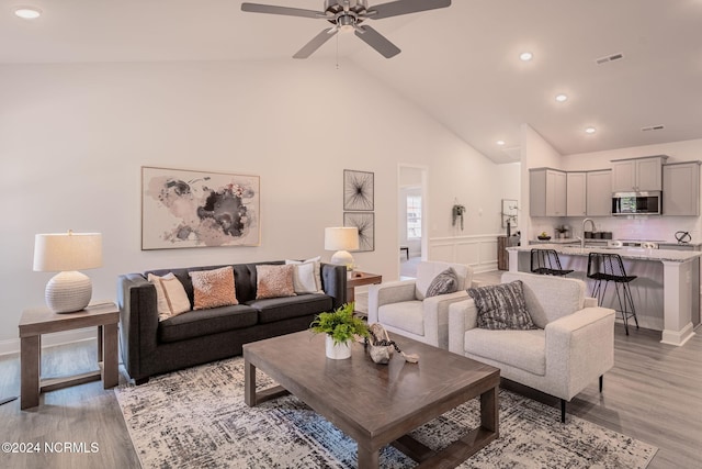 living room with ceiling fan, sink, light hardwood / wood-style floors, and high vaulted ceiling