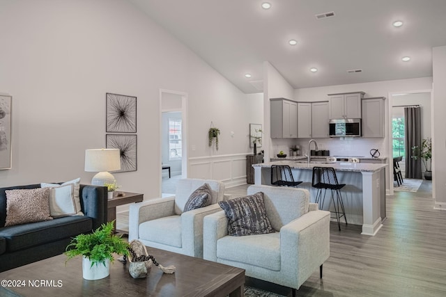 living room with sink, light hardwood / wood-style floors, high vaulted ceiling, and a healthy amount of sunlight