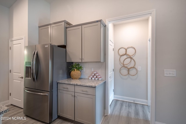 kitchen with tasteful backsplash, gray cabinetry, stainless steel refrigerator with ice dispenser, light stone countertops, and light hardwood / wood-style floors