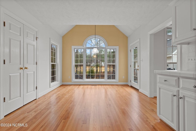 unfurnished dining area featuring lofted ceiling, a textured ceiling, and light hardwood / wood-style flooring