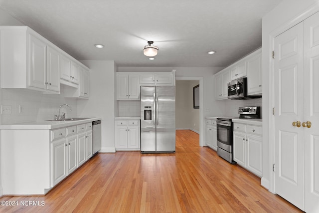 kitchen with appliances with stainless steel finishes, tasteful backsplash, sink, light hardwood / wood-style flooring, and white cabinets