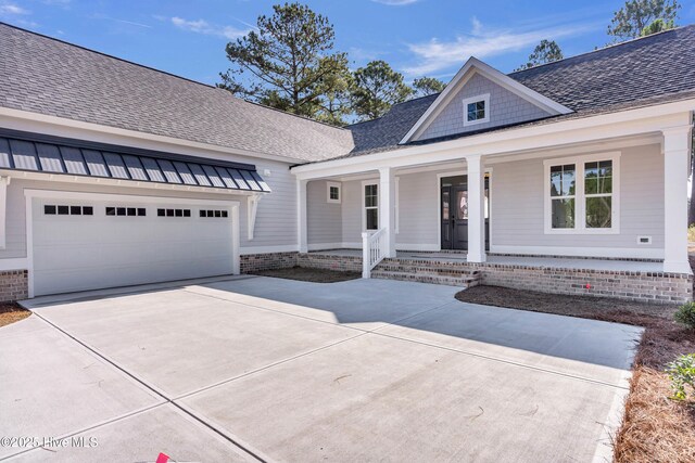 view of front facade with a garage, roof with shingles, a porch, and driveway