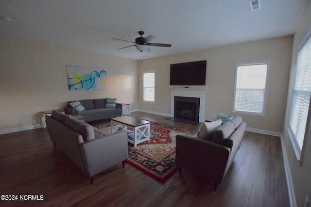 living area featuring a healthy amount of sunlight, a fireplace with flush hearth, visible vents, and wood finished floors