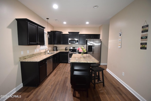 kitchen with hardwood / wood-style flooring, stainless steel appliances, sink, light stone counters, and a kitchen island