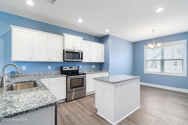 kitchen featuring a center island, sink, white cabinetry, hanging light fixtures, and stainless steel appliances