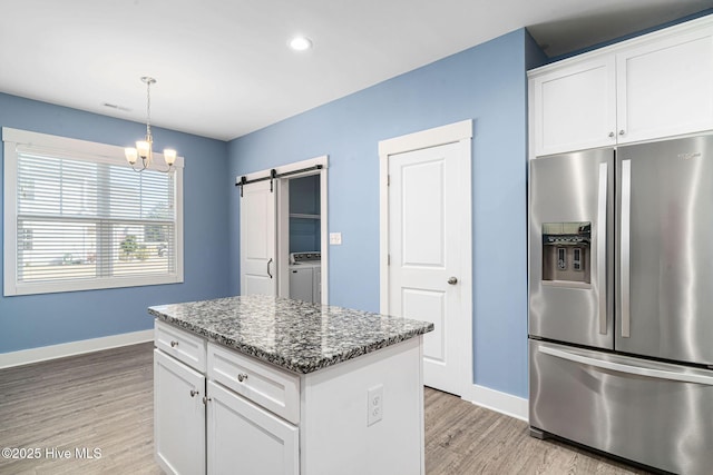 kitchen featuring white cabinets, stainless steel fridge with ice dispenser, a barn door, and washer / clothes dryer