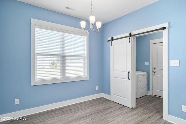 spare room featuring washer / dryer, light hardwood / wood-style floors, a barn door, and a notable chandelier