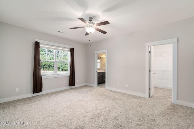 unfurnished bedroom featuring a spacious closet, connected bathroom, a closet, ceiling fan, and light colored carpet