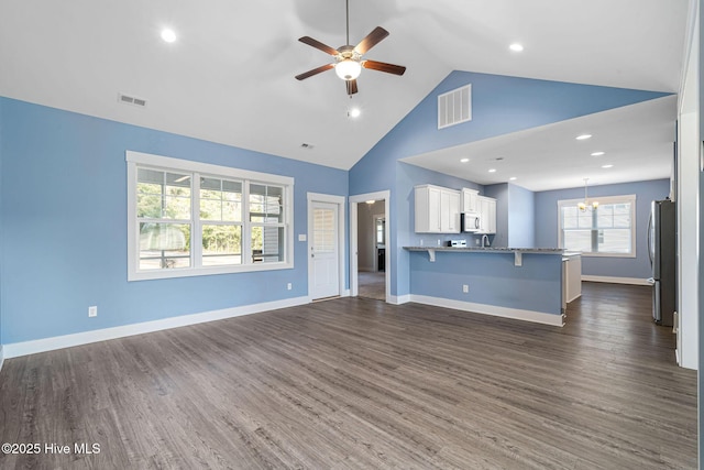 unfurnished living room with ceiling fan with notable chandelier, dark hardwood / wood-style floors, and high vaulted ceiling