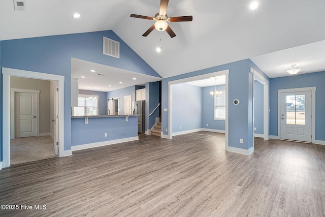 unfurnished living room with a healthy amount of sunlight, ceiling fan with notable chandelier, hardwood / wood-style floors, and high vaulted ceiling