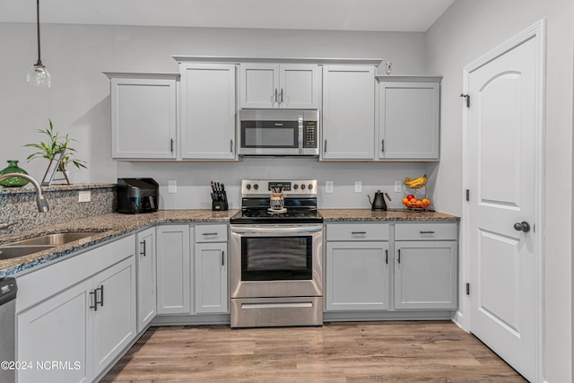 kitchen with stone counters, appliances with stainless steel finishes, sink, light wood-type flooring, and decorative light fixtures