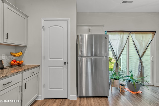 kitchen with white cabinets, light stone counters, light wood-type flooring, and stainless steel fridge