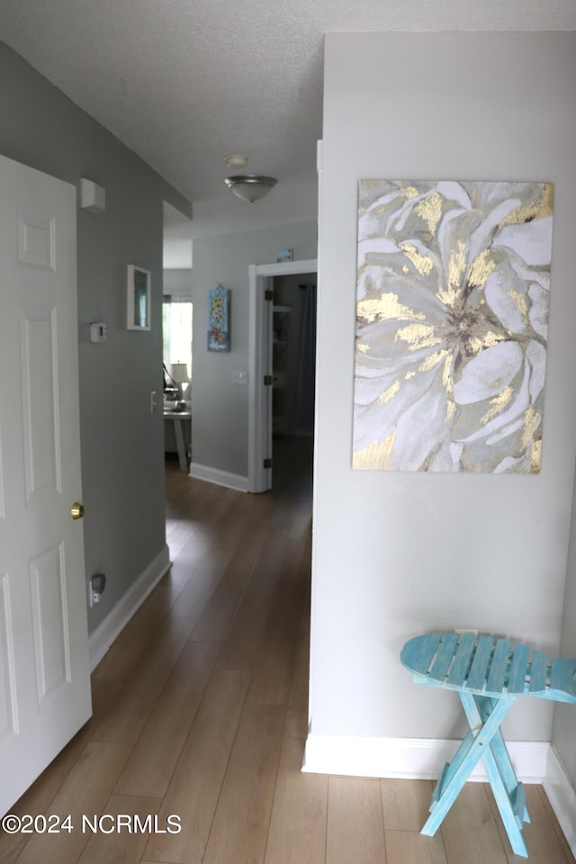 corridor with a textured ceiling and hardwood / wood-style flooring