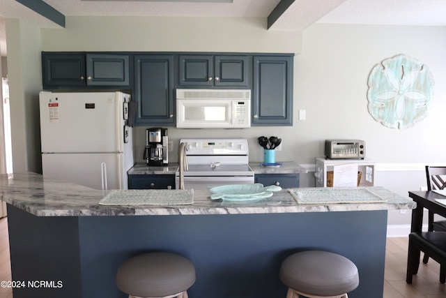 kitchen featuring stone counters, a breakfast bar, and white appliances