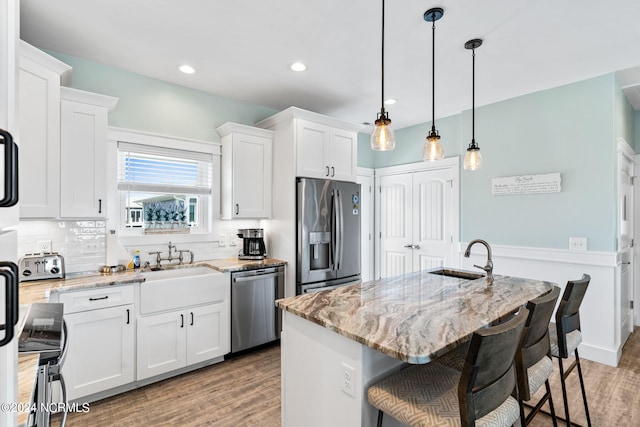 445 E Third St, Ocean Isle Beach, NC 28469 - kitchen featuring stainless steel appliances, a sink, light wood-style floors, white cabinetry, and a breakfast bar area