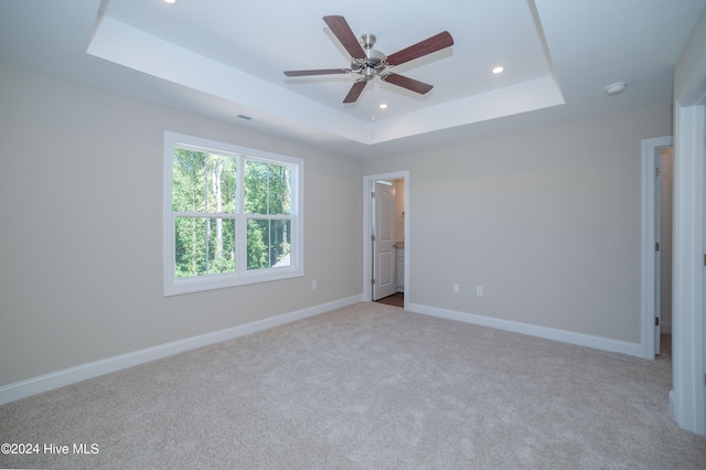 unfurnished bedroom featuring ceiling fan, a raised ceiling, and light colored carpet