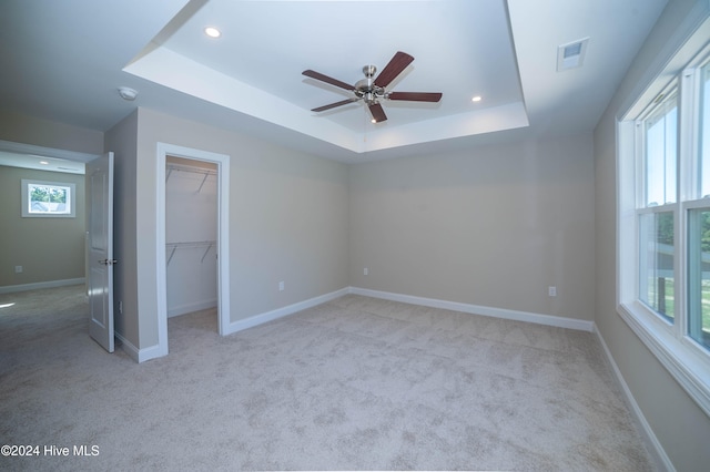 unfurnished bedroom featuring ceiling fan, light colored carpet, a tray ceiling, a walk in closet, and a closet