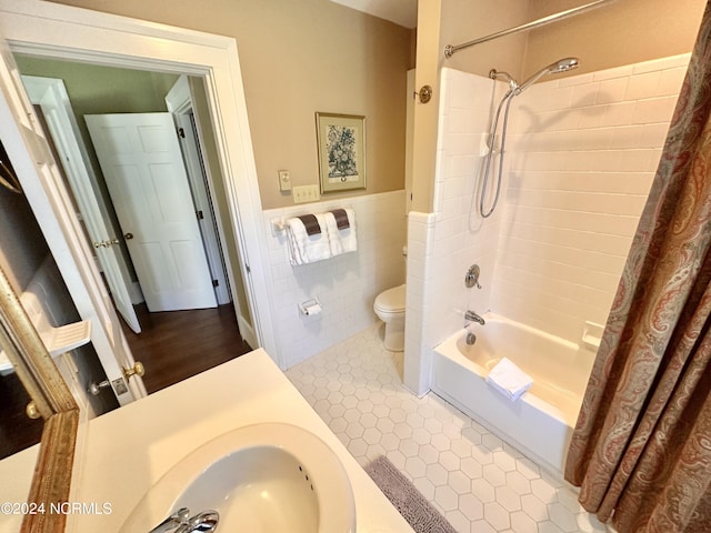 bathroom with a wainscoted wall, tile walls, shower / bathtub combination with curtain, toilet, and tile patterned floors