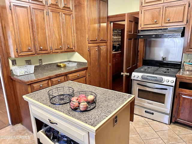 kitchen featuring brown cabinetry, tile countertops, under cabinet range hood, and gas range