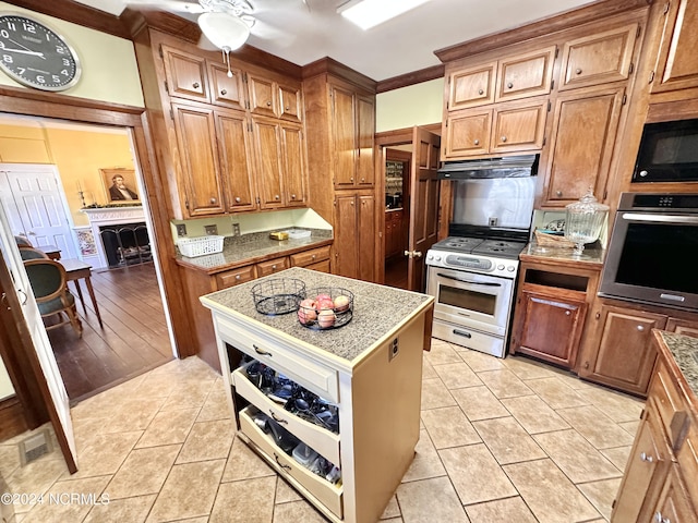 kitchen with light tile patterned floors, brown cabinetry, appliances with stainless steel finishes, a center island, and under cabinet range hood