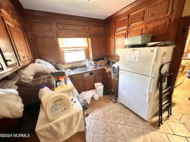 kitchen with brown cabinetry, freestanding refrigerator, light countertops, and a sink