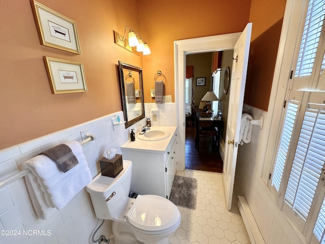 bathroom with a wainscoted wall, tile walls, toilet, vanity, and tile patterned floors