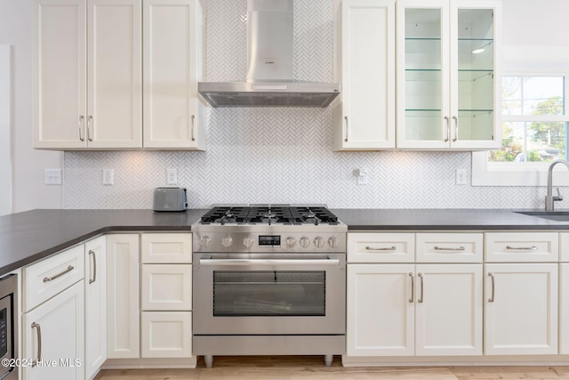 kitchen with wall chimney exhaust hood, backsplash, appliances with stainless steel finishes, white cabinets, and light wood-type flooring