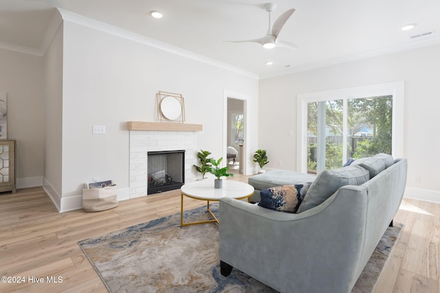 living room with a fireplace, light wood-type flooring, ceiling fan, and crown molding