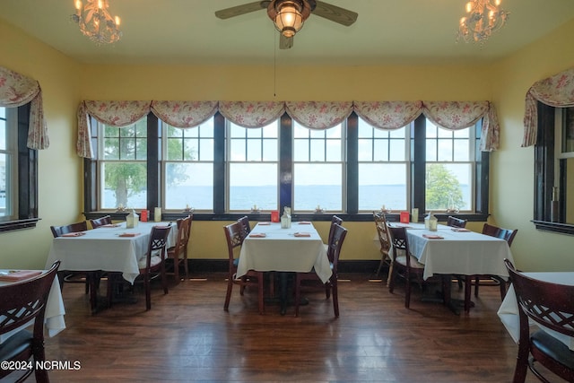 dining room with ceiling fan with notable chandelier, dark hardwood / wood-style flooring, and a water view