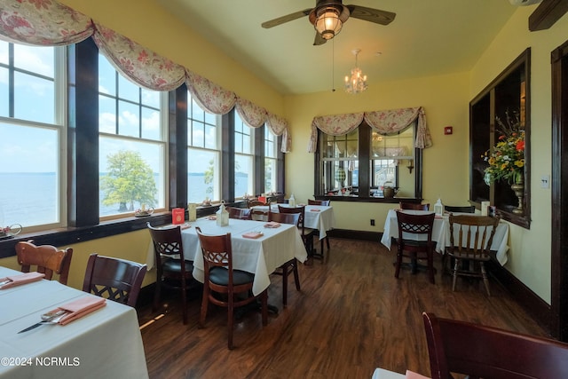 dining area with ceiling fan with notable chandelier, a water view, and dark hardwood / wood-style floors