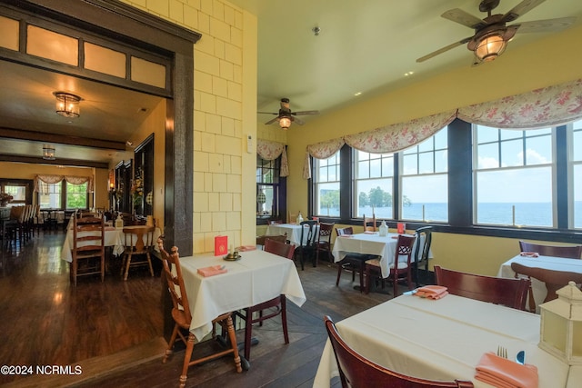 dining space featuring ceiling fan, a water view, and dark wood-type flooring