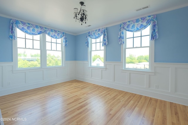 spare room featuring a notable chandelier, light wood-type flooring, and ornamental molding